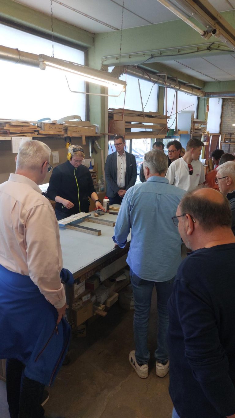 Unternehmensvorstellung Sokol Küchen Hausen Eine Gruppe von Personen steht um einen Tisch in einer Werkstatt.